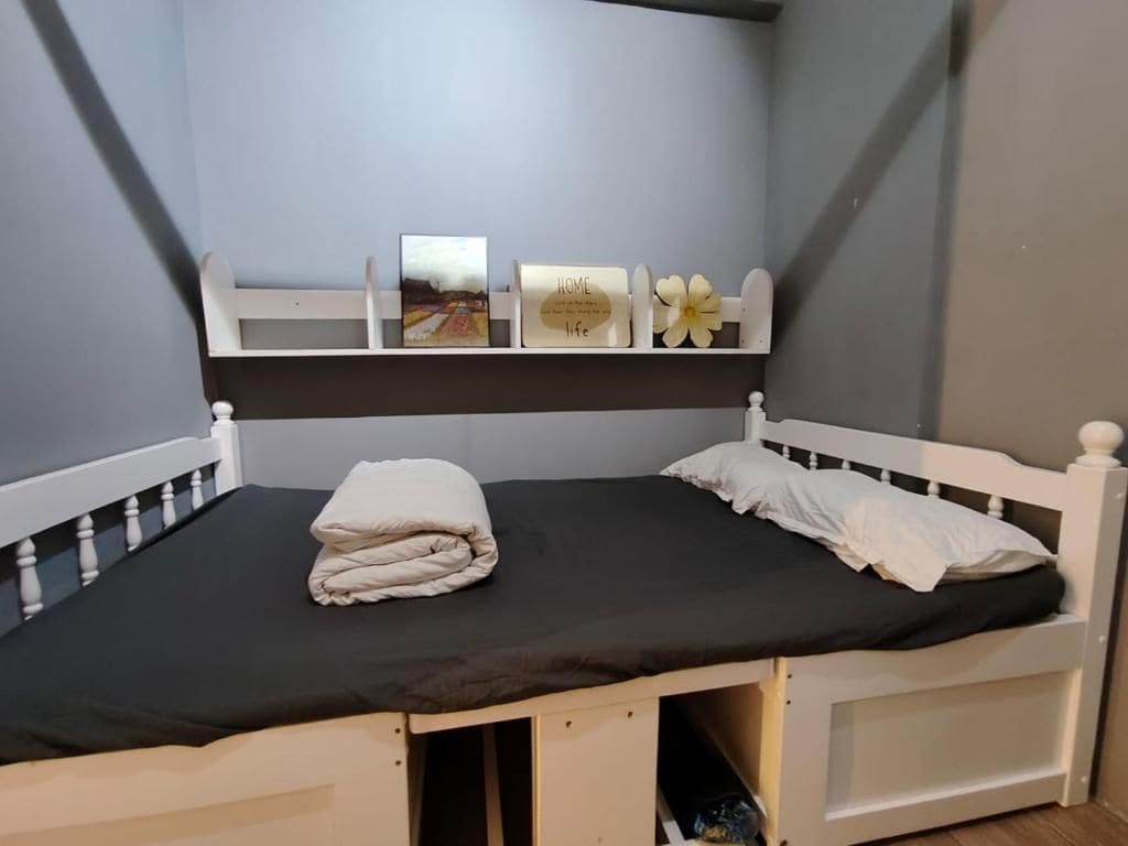 A single bed with a white headboard and footboard, a black mattress, and a folded white blanket.