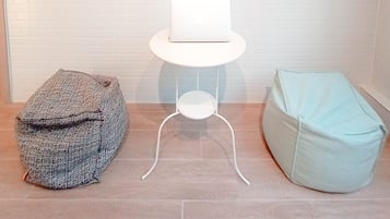 A room with a white brick wall, a clock, a framed picture, a laptop on a small white table, and two bean bags.