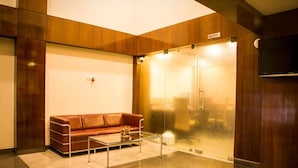 Een moderne lobby met een leren bank, een glazen bijzettafeltje en een glazen deuropening voor de lift.