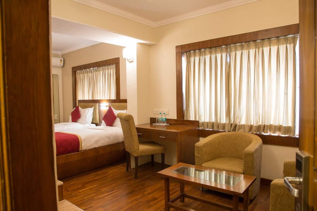 Ein Hotelzimmer mit Bett, Schreibtisch, Stuhl, kleinem Tisch und einem Fenster mit Vorhängen.