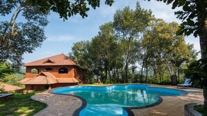 A swimming pool with a curved edge, surrounded by a brick patio and a small brick building with arched windows. - Indeevara Retreat (A unit of Saroma Hill Resorts) (Vythiri)