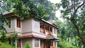 A two-story house with a stone retaining wall, a wooden staircase, and a garden. - Indeevara Retreat (A unit of Saroma Hill Resorts) (Vythiri)