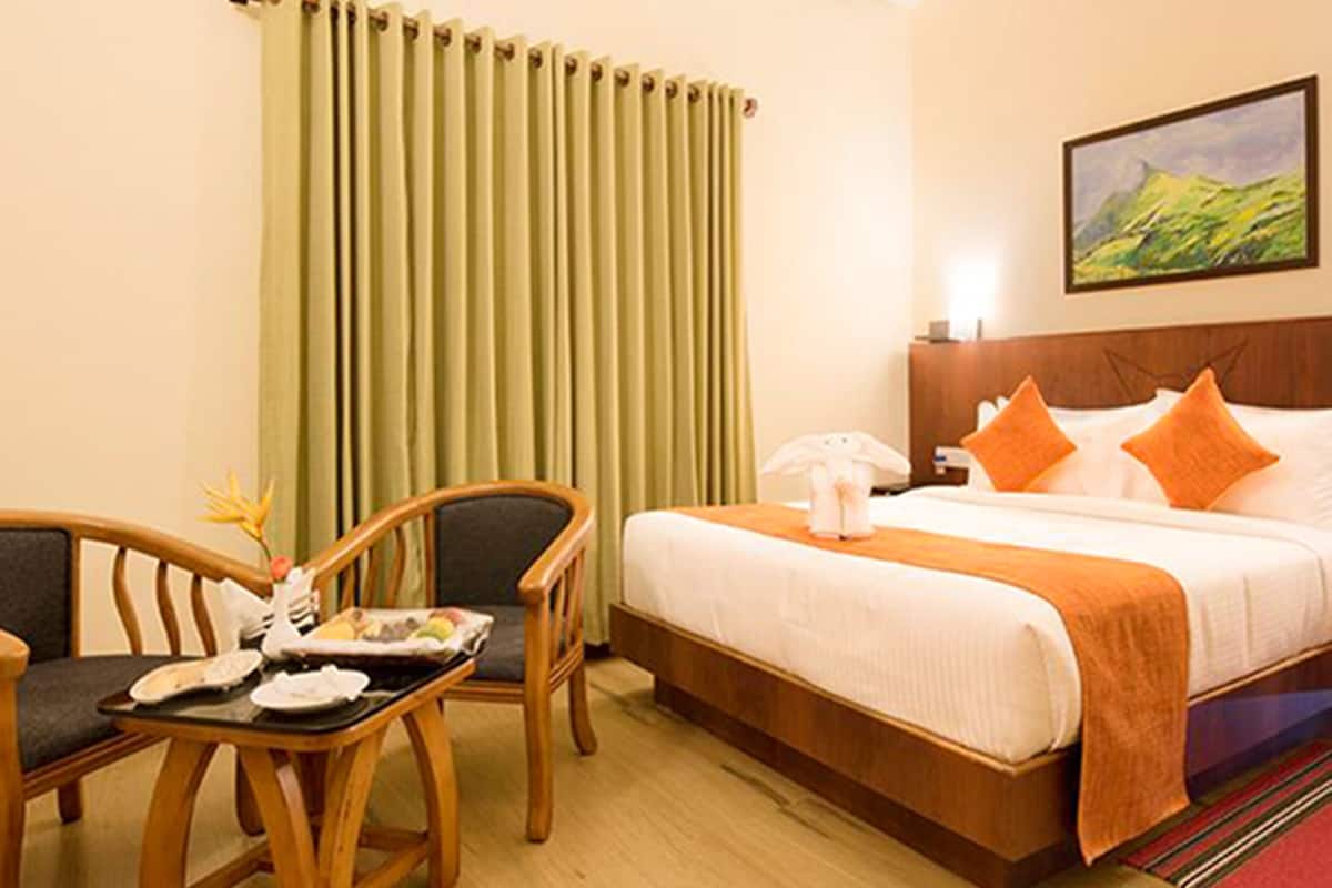 Quarto de hotel com cama, escrivaninha com cadeira, telefone e um quadro na parede.