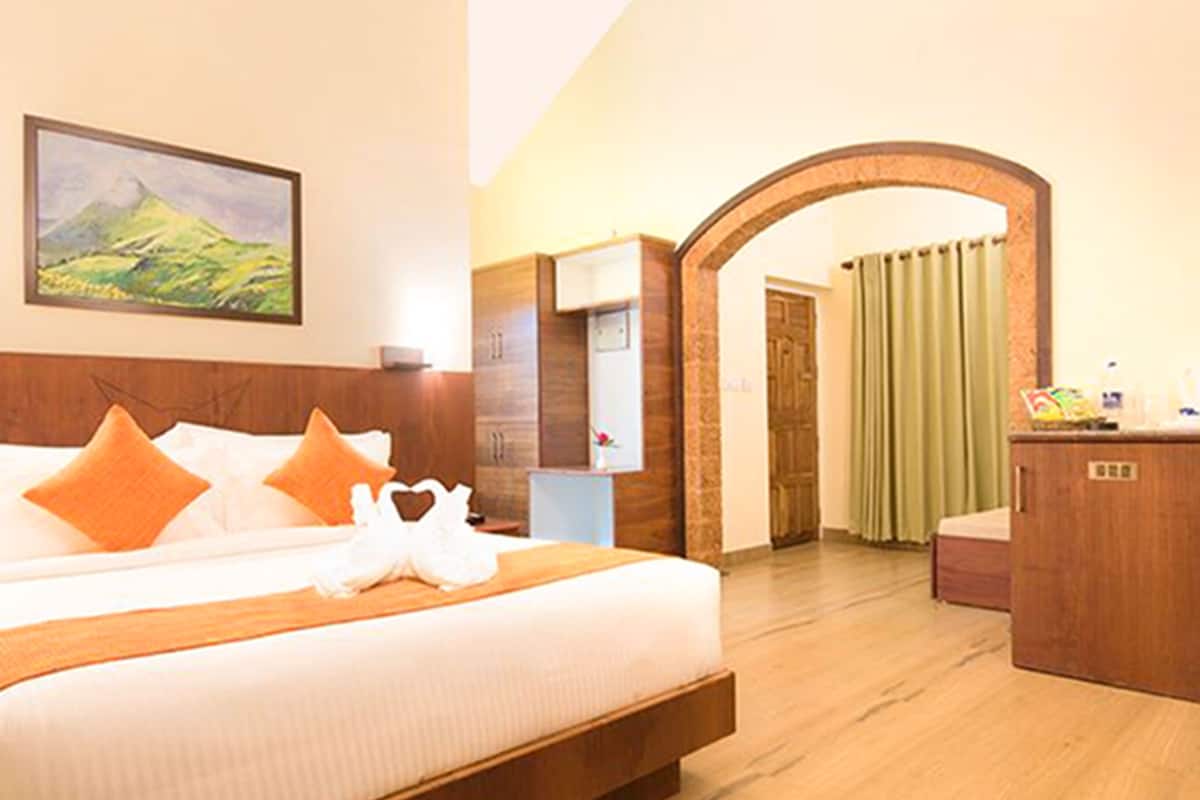 Quarto de hotel com uma cama grande, cabeceira de madeira, um quadro na parede, uma escrivaninha com um espelho e cortina verde.