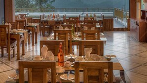 A restaurant with wooden tables and chairs, large windows offering a view of mountains. - Indeevara Retreat (A unit of Saroma Hill Resorts) (Vythiri)
