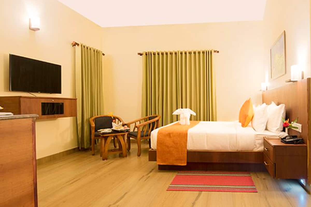 Quarto de hotel com cama, escrivaninha, cadeira, televisão e cortinas.
