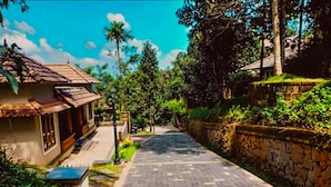 A paved pathway leading to a traditional house with a tiled roof, surrounded by lush greenery and stone walls. - Indeevara Retreat (A unit of Saroma Hill Resorts) (Vythiri)