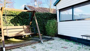 Ein hölzernes Schaukelgestell in einem Garten mit einem weißen Gebäude im Hintergrund.