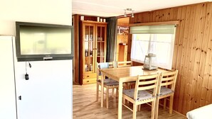 Ein Zimmer mit Holzwandverkleidung, einem Esstisch, Stühlen, einem Schrank und einem Fenster mit Vorhängen.