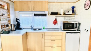 Eine kleine Küche mit Holzausstattung, einem Edelstahl-Spülbecken, einer Mikrowelle und einem kleinen Kühlschrank.