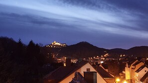 A town at dusk with a hilltop castle illuminated in the distance.