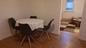 A dining area with a round table covered by a white tablecloth, surrounded by four chairs with wooden legs.
