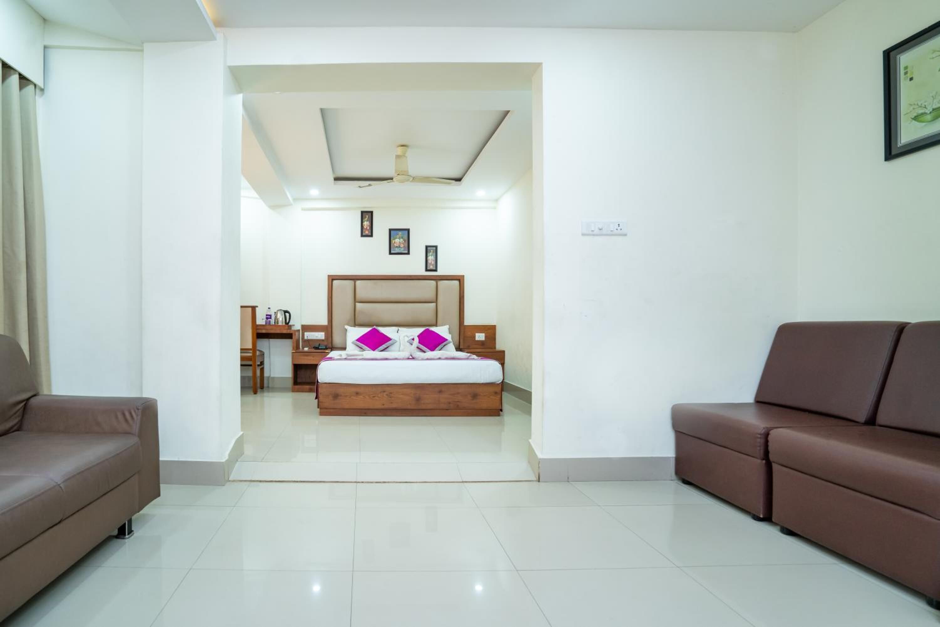 A modern hotel room with a large bed, two sofas, a desk, and a ceiling fan.