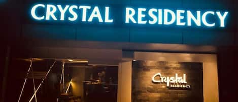 The exterior of Crystal Residency with a prominent neon sign and a modern facade.