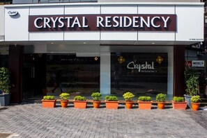 Exterior del Crystal Residency con un letrero visible, plantas en macetas al frente y un área de entrada pavimentada.