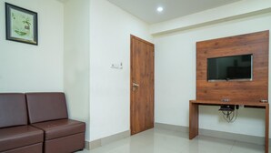 Une pièce avec un canapé en cuir marron, une porte en bois, un téléviseur fixé sur un meuble en bois et un sol carrelé.