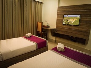 Habitación de hotel con dos camas, un escritorio, una silla y un televisor montado en la pared.