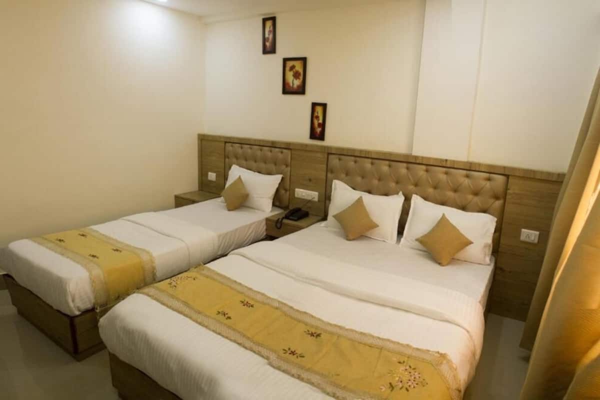 Ein Hotelzimmer mit zwei Betten, jeweils mit Kopfteil, weißer Bettwäsche und gelbem Zierstreifen. An der Wand über den Betten hängen drei gerahmte Bilder.