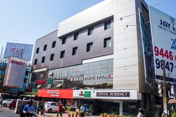 Un edificio moderno con varias fachadas comerciales, incluyendo una oficina de Rolex Travel & Tours, Crystal Residency y Boy's Saloon.