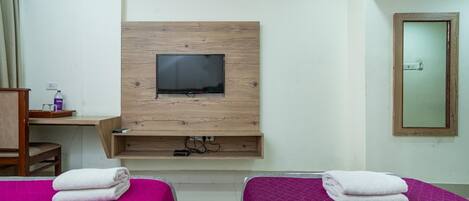 A hotel room with two beds, a TV mounted on a wooden panel, a desk with a chair, and a mirror on the wall.