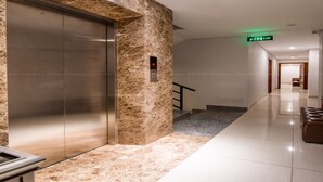 A modern elevator with a marble wall, a digital display, and a hallway leading to a staircase. - GALAXY AIRPORT HOTEL (Ho Chi Minh City)
