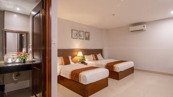 Quarto de hotel com duas camas, banheiro com espelho, pia e vaso sanitário, e um aparelho de ar condicionado na parede.