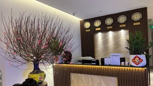 A reception desk with clocks displaying different time zones, a vase with pink flowers, and a potted plant. - GALAXY AIRPORT HOTEL (Ho Chi Minh City)