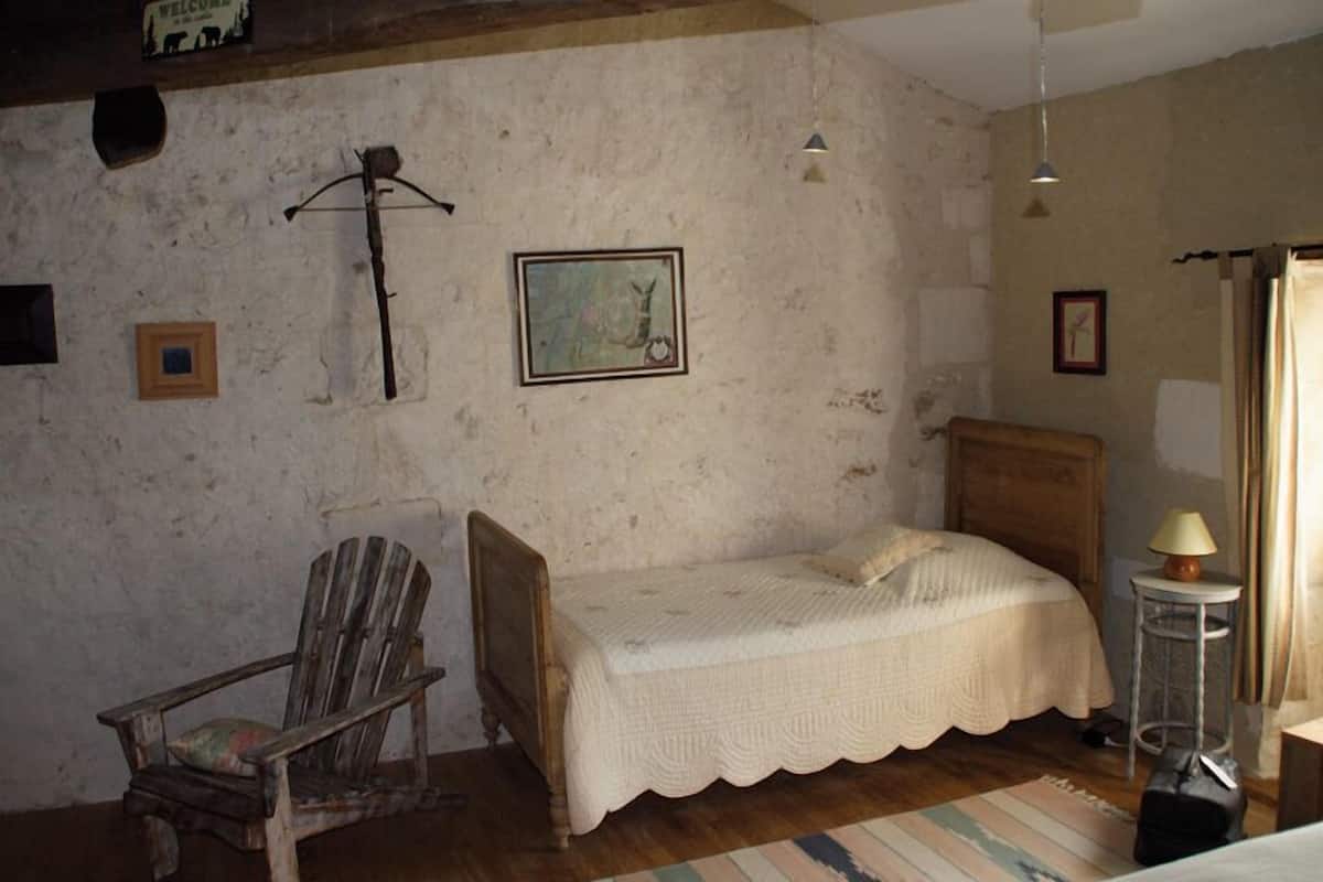 Una habitación rústica con una cama de madera, una silla, una mesita con una lámpara y un cuadro en la pared.