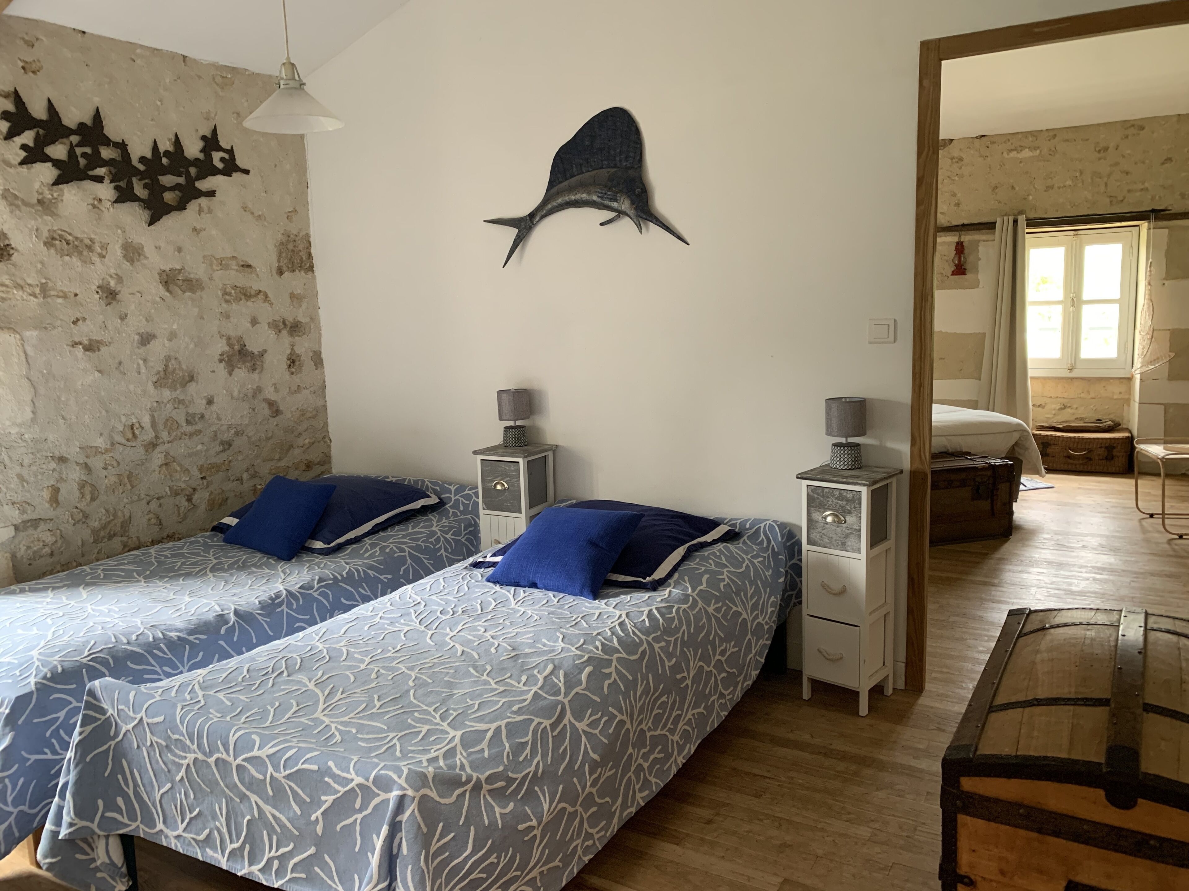 A bedroom with two beds, a wall-mounted fish decoration, bedside tables with lamps, and a wooden chest.