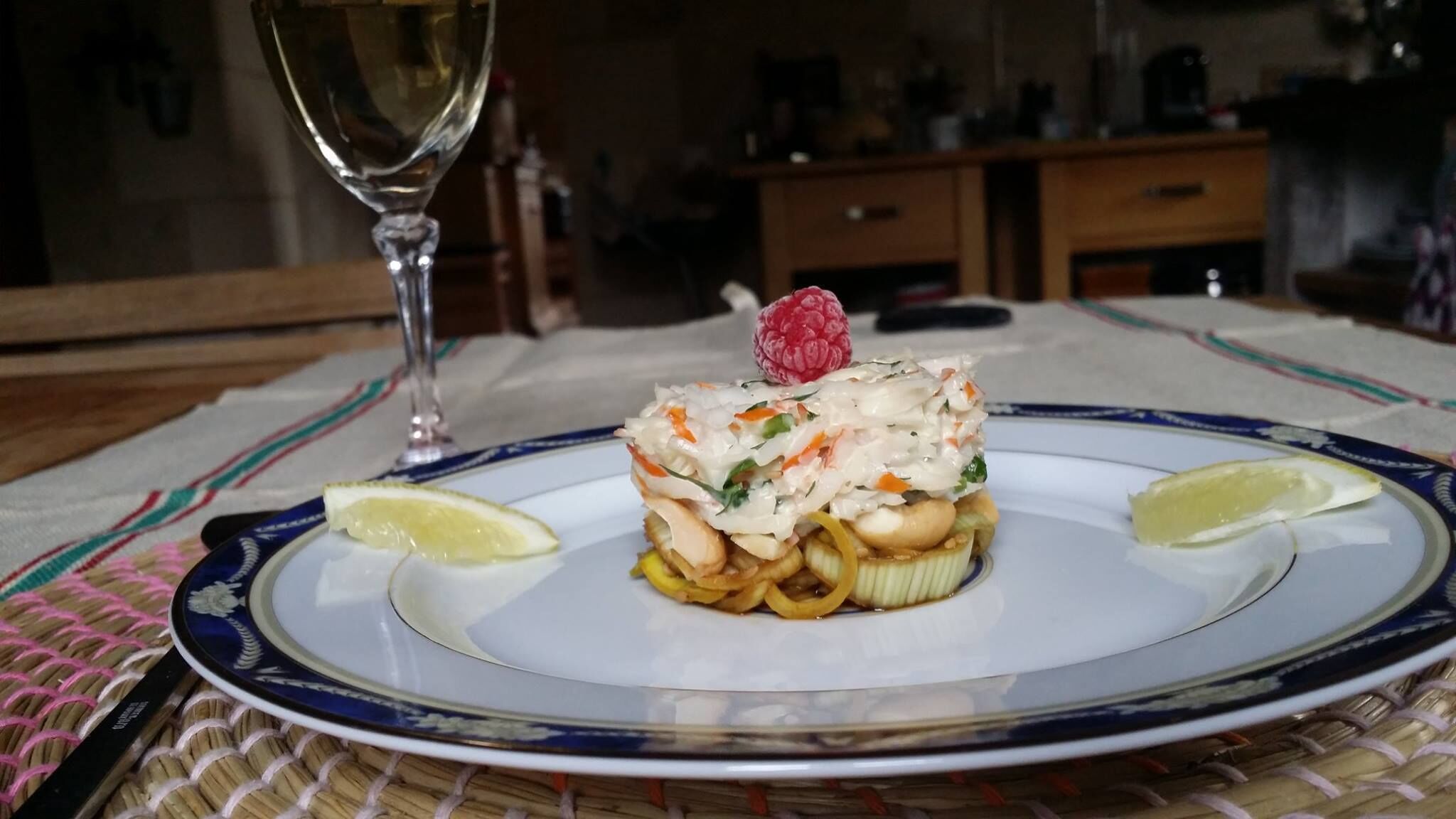A plate of seafood salad with lemon wedges and a raspberry on a table with a woven placemat.