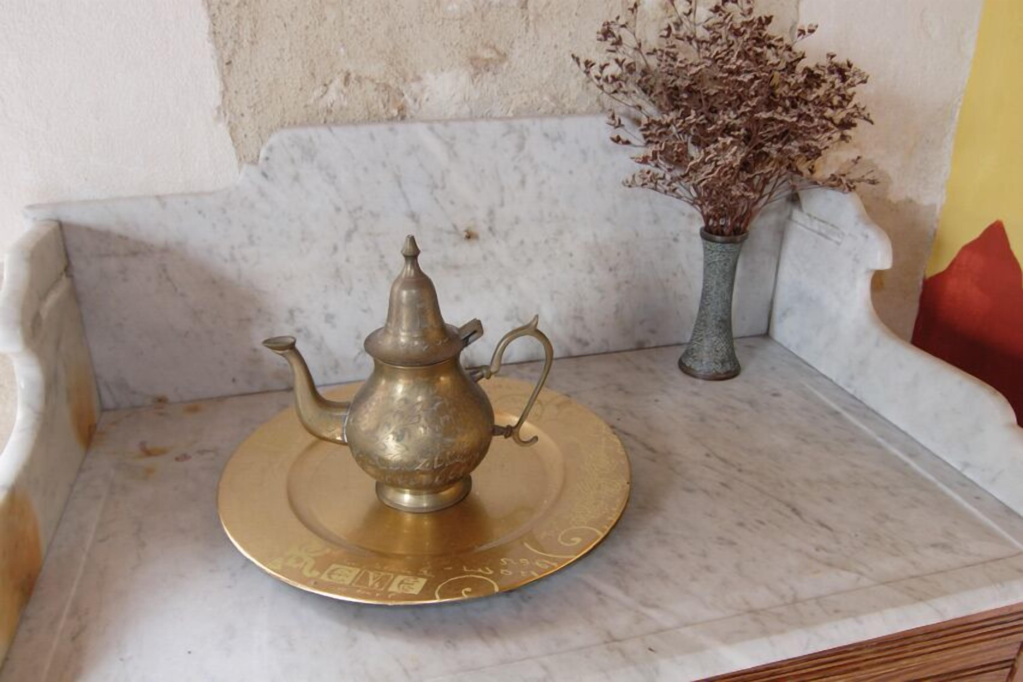A brass teapot on a marble surface with a decorative plate.
