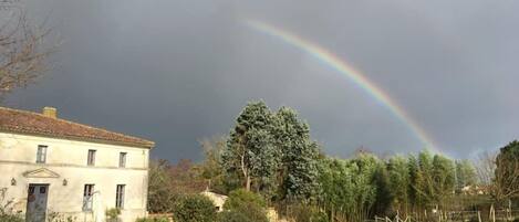 Una casa con jardín, un arcoíris y un cielo nublado.