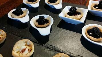 A slate serving board with small white bowls containing desserts topped with blackberries.