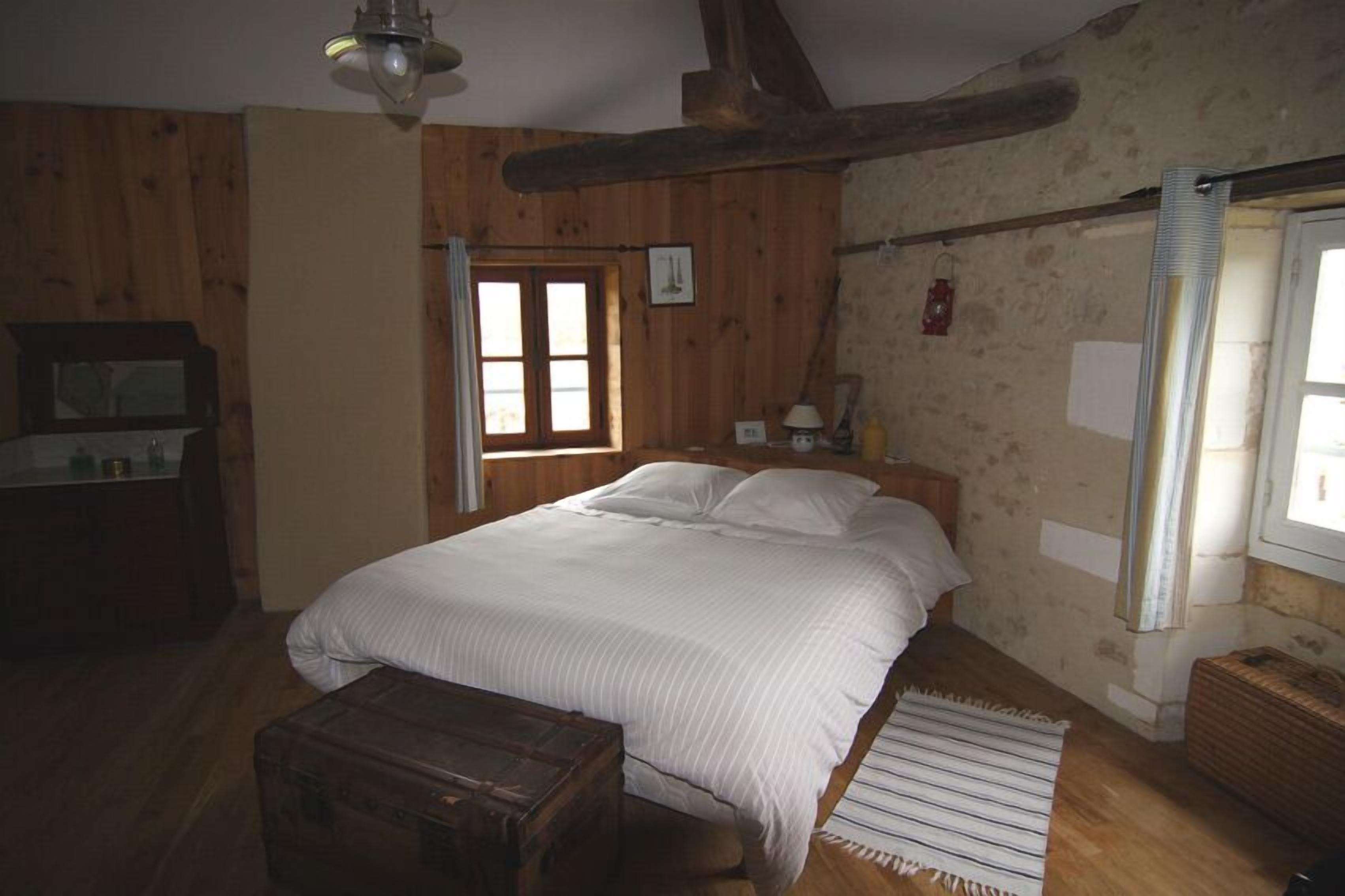Un dormitorio con paneles de madera, una cama, una mesita de noche, un tocador y una ventana con cortinas.