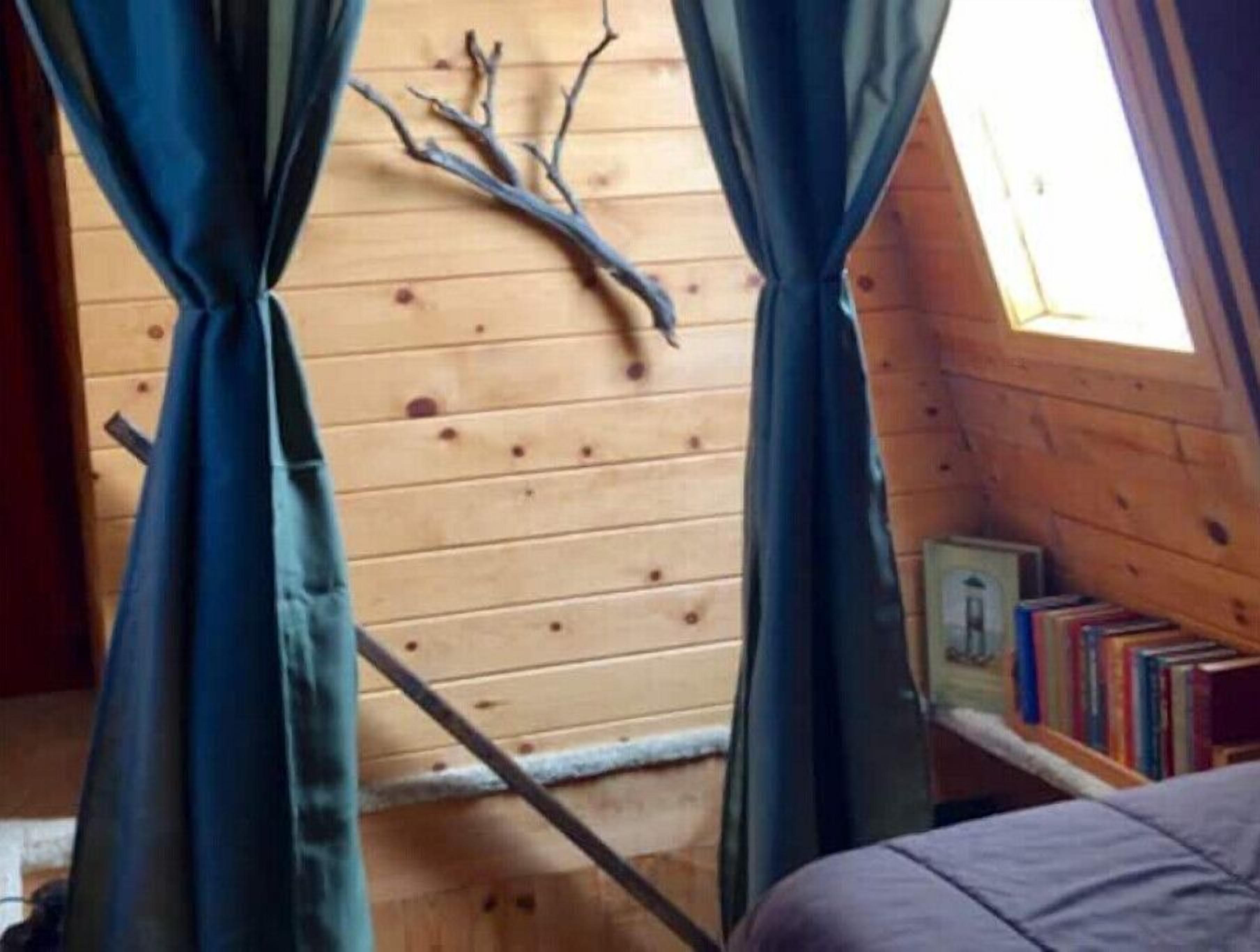 A cozy room with wooden walls, a window with curtains, a bed, and a bookshelf.
