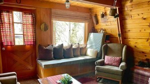 Een gezellig cabin interieur, met houten details, een bank met kussens, een schommelstoel en een tafeltje met een plantje.