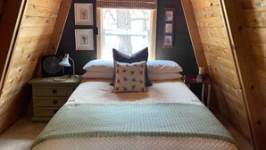 Een gezellige slaapkamer onder de dakpannen, met een bed, nachtkastje, lamp en ingelijste foto's aan de muur.