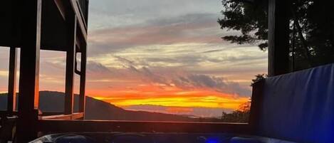Een jacuzzi met blauwe verlichting, uitzicht op een zonsondergang en een berg op de achtergrond.