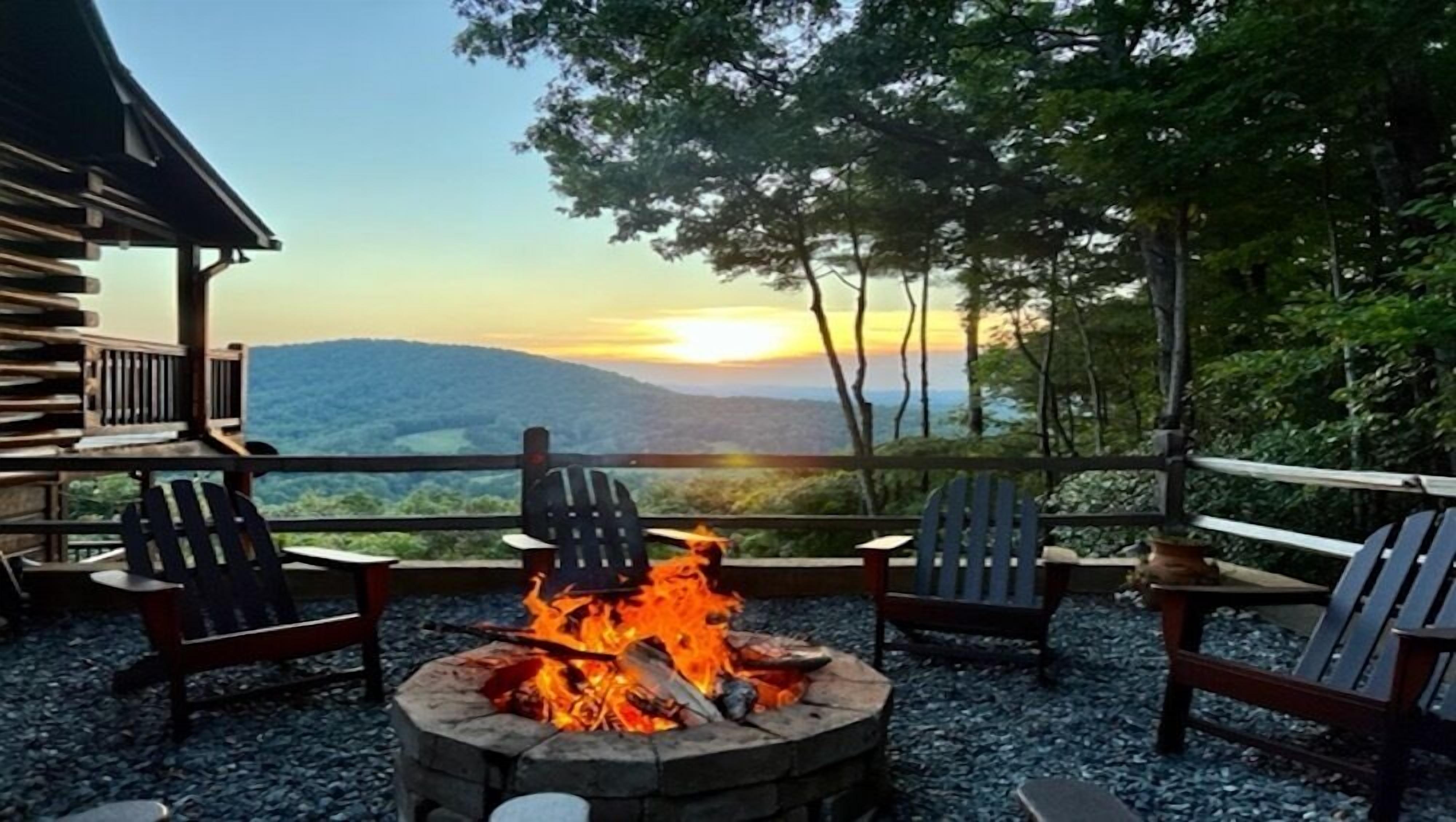 A fire pit with chairs around it, overlooking a scenic view of mountains and a sunset.