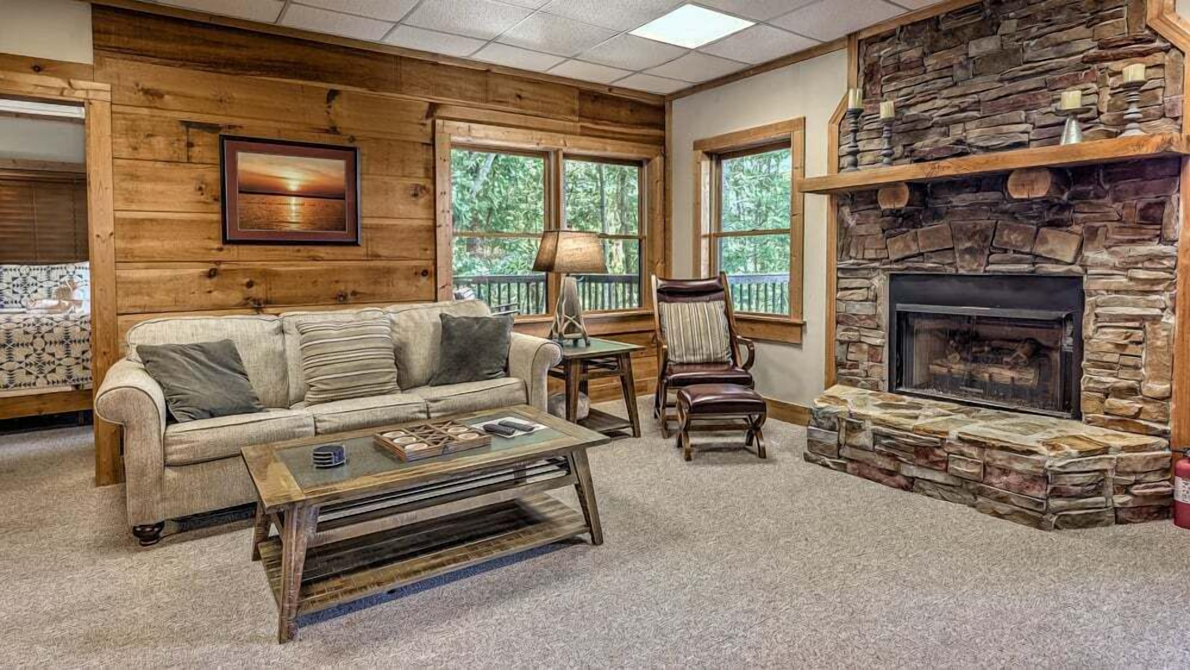 A cozy living room with a stone fireplace, wooden walls, and a comfortable sofa.