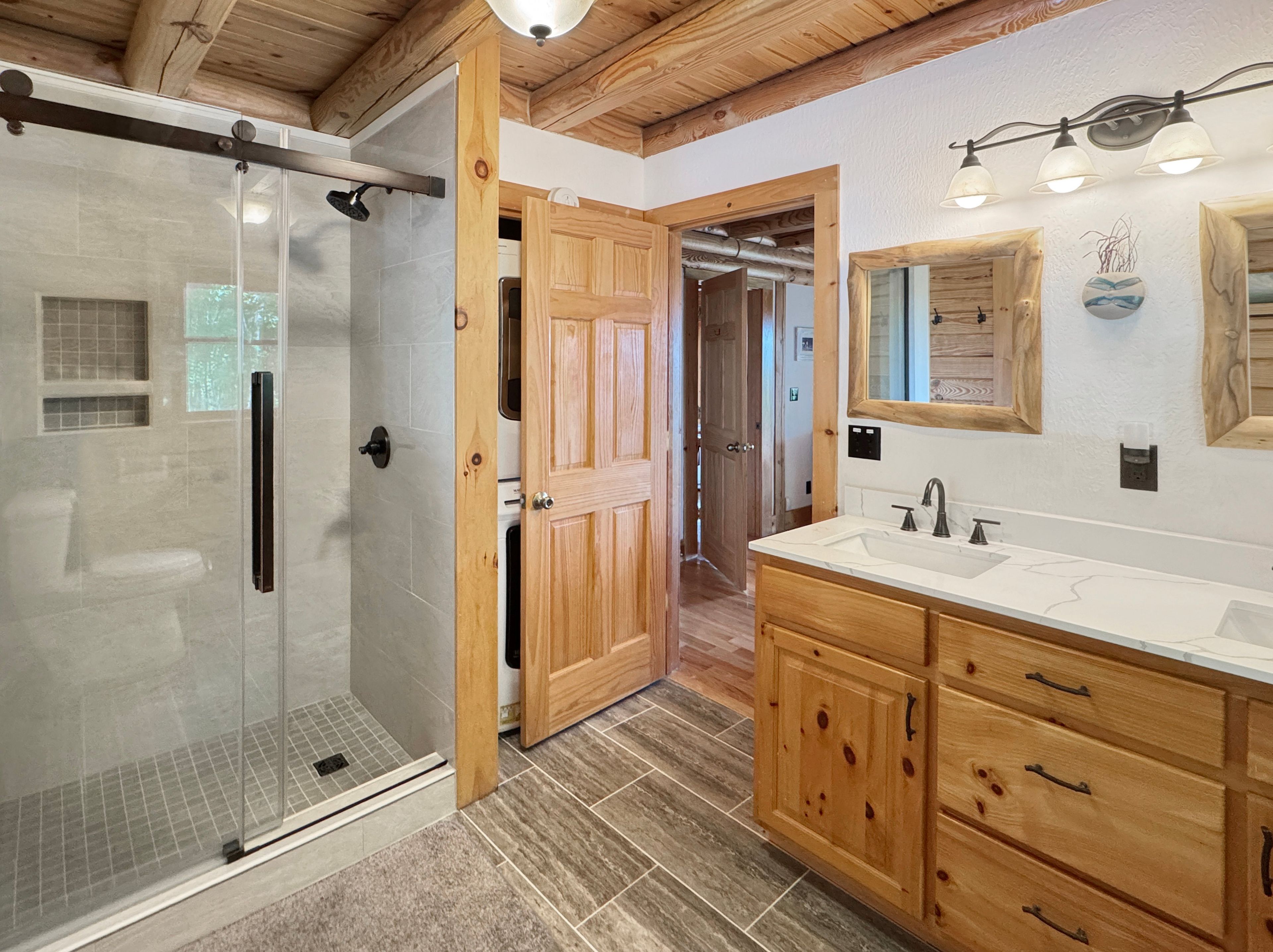 A bathroom with a glass-enclosed shower, wooden cabinets, and a white sink.