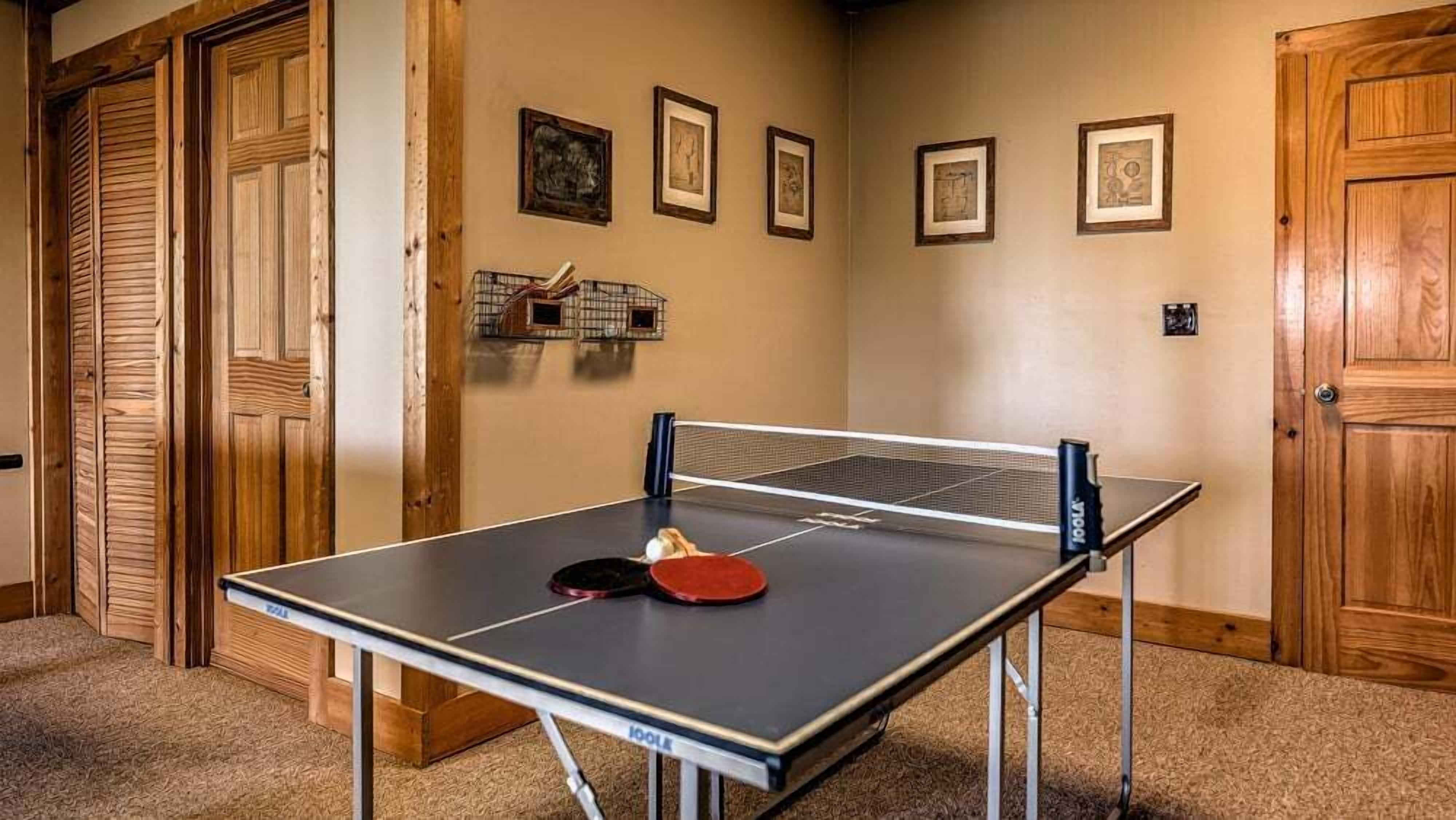 Una mesa de ping pong en una habitación con paredes y puertas de madera, y cuadros enmarcados en la pared.