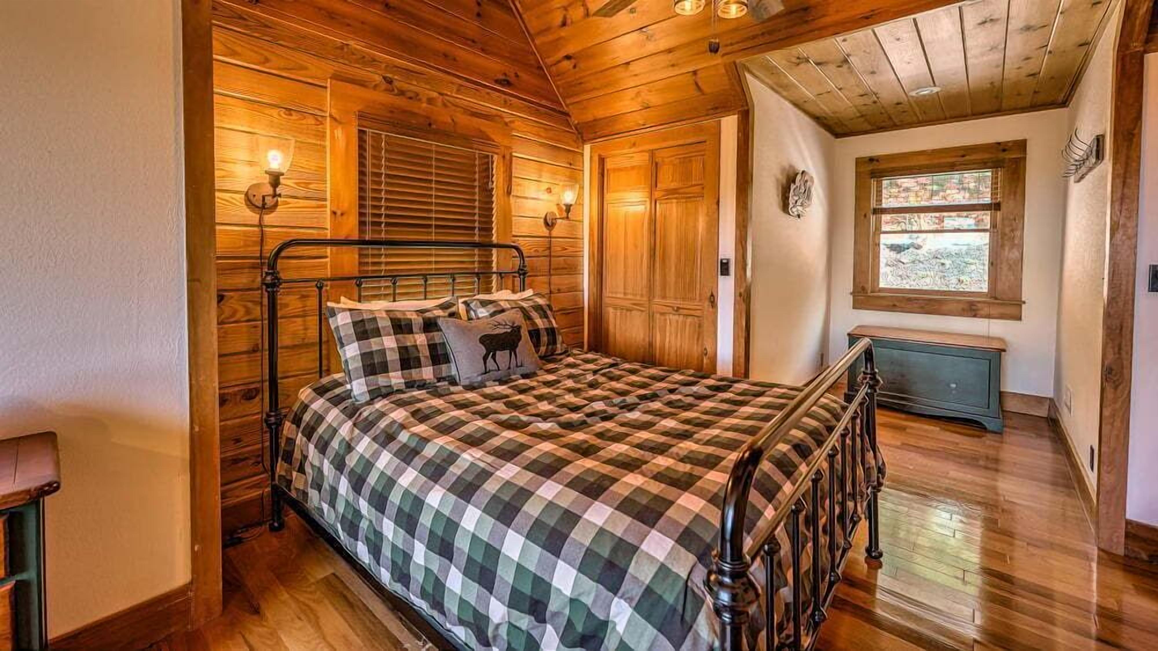 Um quarto aconchegante com estrutura de cama de madeira, roupa de cama xadrez e janela com vista.