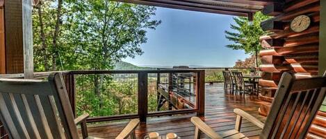 Une terrasse en bois avec des fauteuils Adirondack et une table, donnant sur une zone boisée.