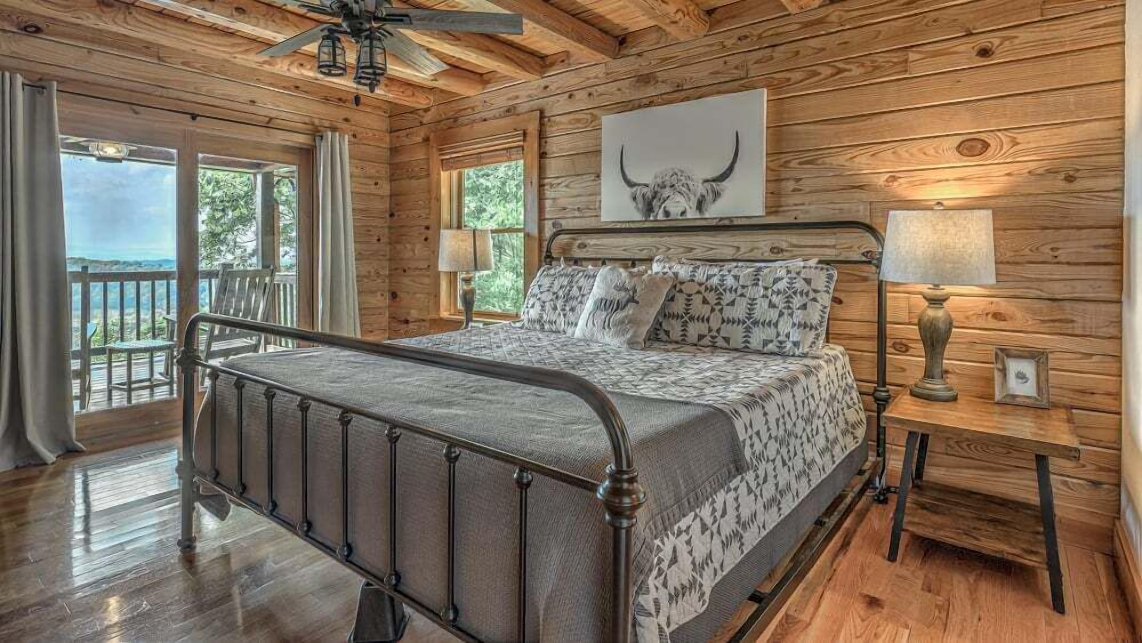 A wooden cabin bedroom with a bed, a nightstand, a lamp, and a ceiling fan.