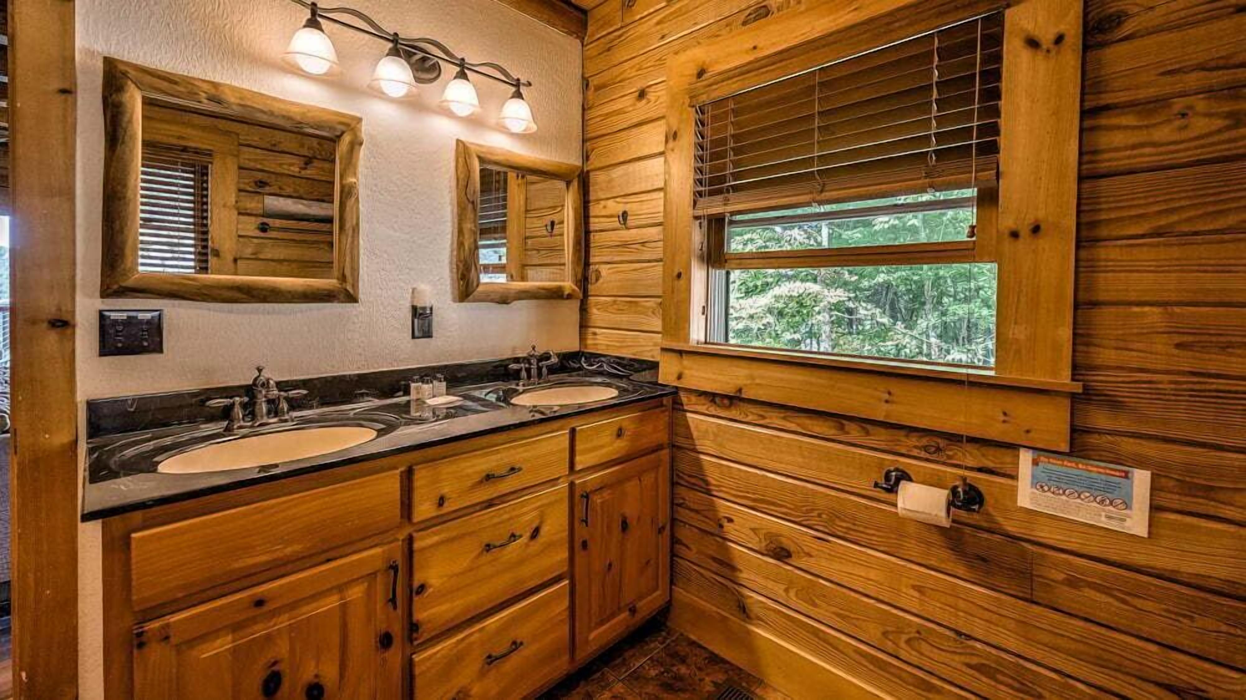 Een houten badkamer in een chalet, met twee wastafels, een spiegel en een raam met zonwering.