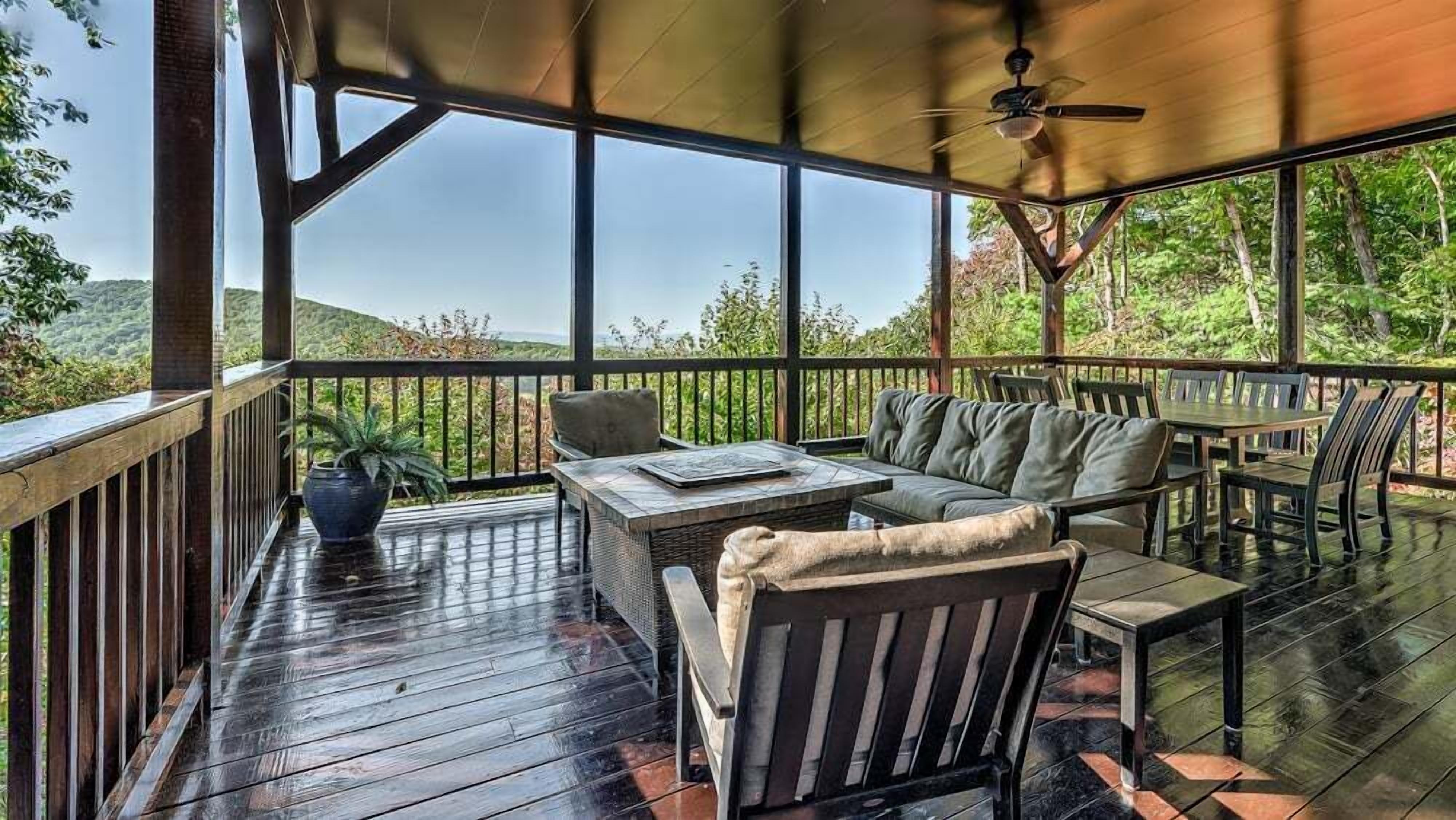 Un espace extérieur abrité, aménagé avec une table et des chaises, un ventilateur de plafond et offrant une vue sur le paysage environnant.