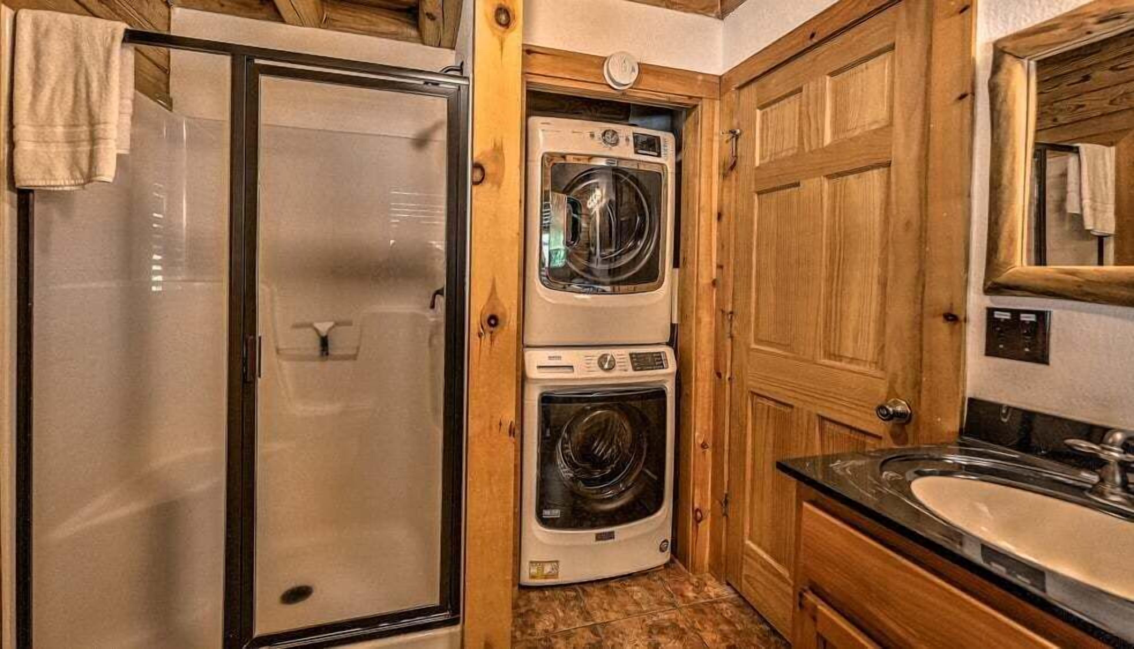 A compact bathroom with a shower, a stacked washer and dryer, and a sink.