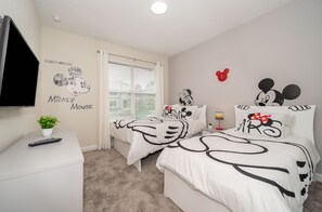 A bedroom with two beds, a TV, and Mickey Mouse-themed decor.