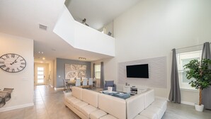 Ein geräumiger Wohnbereich mit einer großen weißen Couch, einem an der Wand befestigten Flachbildfernseher und einem Essbereich mit einem modernen Tisch und Stühlen.